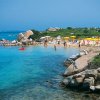Spiaggia rocciosa con ombrelloni gialli e mare cristallino.