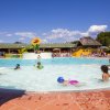 Bambini che giocano in una piscina poco profonda con uno scivolo giallo e verde.