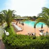 Una grande piscina circondata da lettini e ombrelloni, con palme e persone che si rilassano al sole.