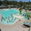 Piscina affollata con scivolo giallo e ombrelloni.