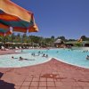 Piscina all'aperto con ombrelloni colorati e bagnanti in una giornata di sole.