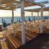 Tavoli e sedie sotto una pergola bianca sulla spiaggia, vista mare al tramonto.