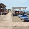 Sdraio e ombrelloni su una spiaggia, vicino a un bar e una sala con tavoli coperti.
