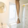 Bagno moderno con lavabo, specchio rotondo, WC e doccia. Finestra con tenda marrone chiusa.