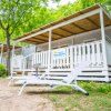 Strutture ricettive con veranda in legno e sdraio, circondate da alberi.