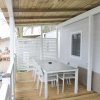 Veranda in legno con tavolo e sedie bianche, pareti chiare e finestre.