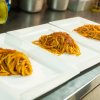 Tre piatti rettangolari con spaghetti al sugo su una superficie di cucina.