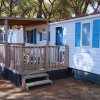 Esterno di un bungalow bianco con persiane blu e veranda in legno, situato in un'area boschiva.