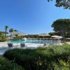 Sdrai e ombrelloni bianchi accanto a una piscina circondata da alberi e piante verdi.