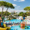 Parco acquatico con piscine azzurre, scivoli gialli e alberi alti.