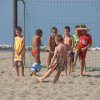 Bambini giocano a calcio in spiaggia, un bambino calcia la palla verso una piccola porta.
