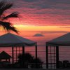 Un tramonto sul mare con tende e una palma in primo piano.