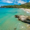 Spiaggia sabbiosa con mare turchese e scogliere verdi.