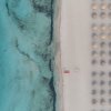 Spiaggia vista dall'alto con file di ombrelloni e mare azzurro.