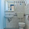 Un bagno piastrellato con lavabo, wc, specchio e asciugacapelli. Doccia con tenda azzurra visibile.
