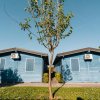 Due bungalow blu affiancati, con un albero davanti e cieli blu chiaro.