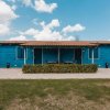 Edificio blu con tetto in tegole, circondato da siepi e un vialetto pavimentato.