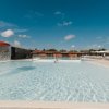 Piscina con fontana a fungo, sdraio e cielo sereno con alcune nuvole.
