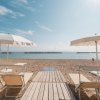 Spiaggia sabbiosa con ombrelloni bianchi e lettini, mare e cielo limpido all'orizzonte.