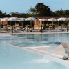 Piscina con cascata d'acqua, lettini e ombrelloni bianchi.