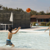 Tre bambini giocano a palla in una piscina all'aperto.