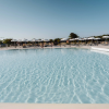 Una piscina scintillante sotto un cielo azzurro con ombrelloni bianchi sullo sfondo.