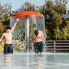 Due ragazzi giocano sotto una fontana a forma di fungo in piscina.