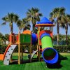 Parco giochi colorato con scivolo e palme sullo sfondo.
