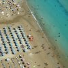 Vista aerea di spiaggia affollata con ombrelloni e mare turchese.