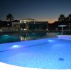 Piscina illuminata al tramonto con palme.