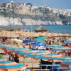 Spiaggia affollata di ombrelloni colorati, città sullo sfondo.