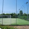 Campo da calcetto con rete recintata e vegetazione sullo sfondo.