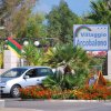 Ingresso di Villaggio Arcobaleno con auto e aiuole fiorite.