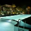 Piscina illuminata di notte, circondata da palme.