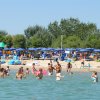 Spiaggia affollata con gente che nuota e ombrelloni blu.