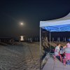 Spiaggia di notte con gazebo e persone sedute.