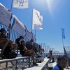 Spettatori seduti su gradinate all'aperto con bandiere sopra.