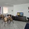 Sala con tavoli rotondi e sedie di vimini, TV su mobile scuro e scaffale con decorazioni.
