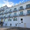 Edificio bianco a più piani con balconi, cielo azzurro e nuvole.