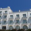 Edificio bianco a tre piani con balconi e cielo azzurro.