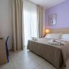 Camera da letto semplice con letto matrimoniale, parete lilla e finestra con tenda bianca.